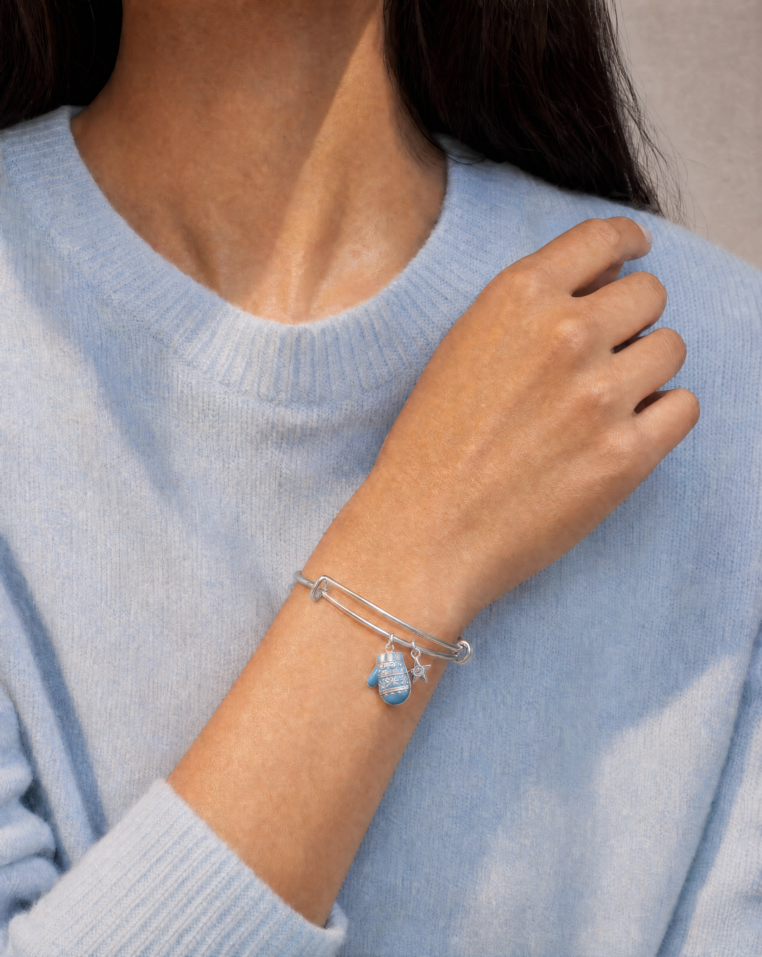 A close-up of a person wearing a delicate silver wire charm bracelet with a small blue sea otter charm, paired with a light blue knit sweater.