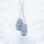 A silver chain necklace with a pair of blue and white patterned mitten-shaped charms, photographed against a soft, snowy white background.