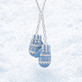 A silver chain necklace with a pair of blue and white patterned mitten-shaped charms, photographed against a soft, snowy white background.