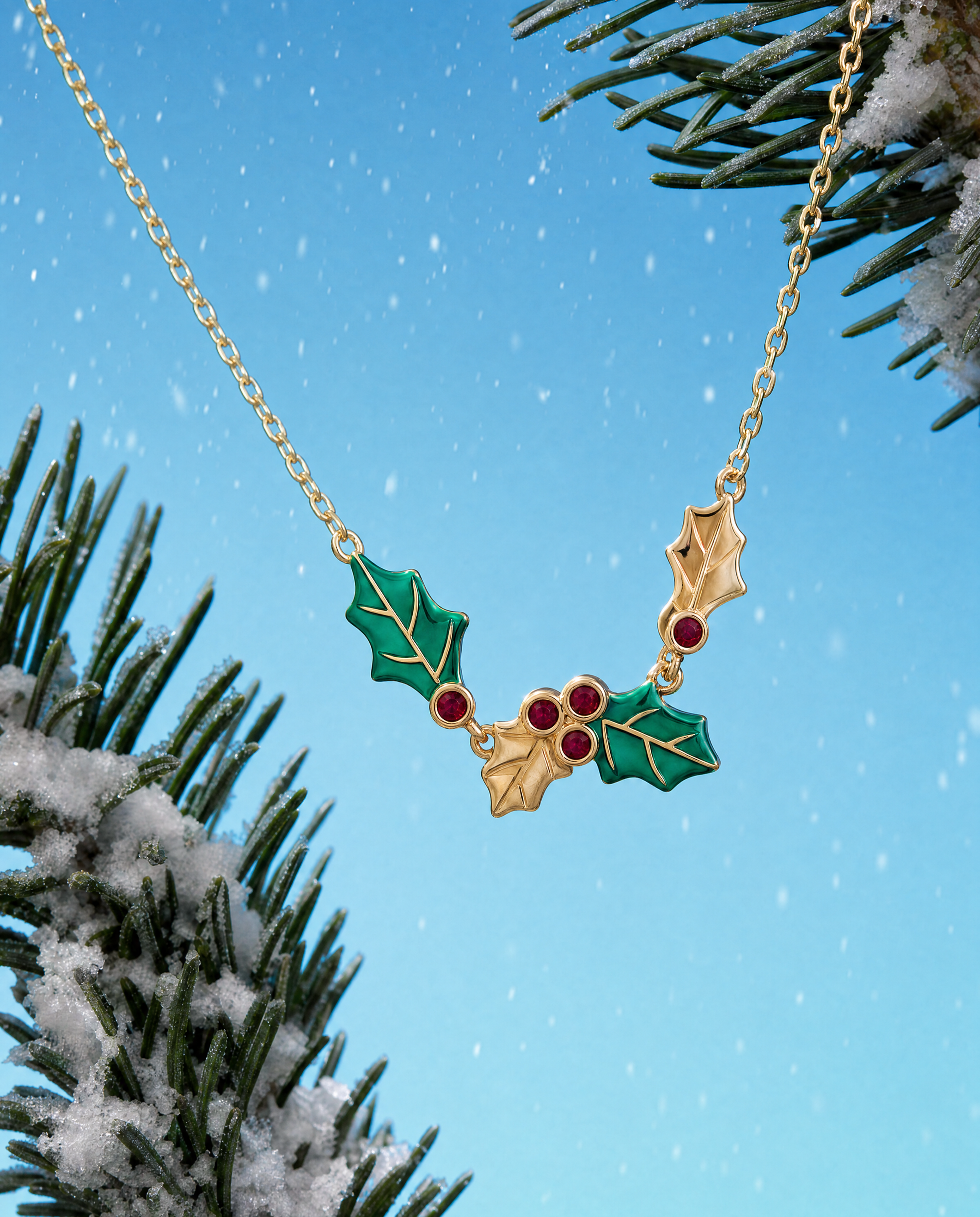 A gold holly necklace with green enamel leaves and red berry accents, shown hanging against a bright blue sky background with snowy pine branches.