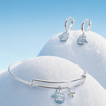 A silver bangle bracelet and matching drop earrings with snowflake and star charms, styled on a blue snowy background on top of two mounds of snow