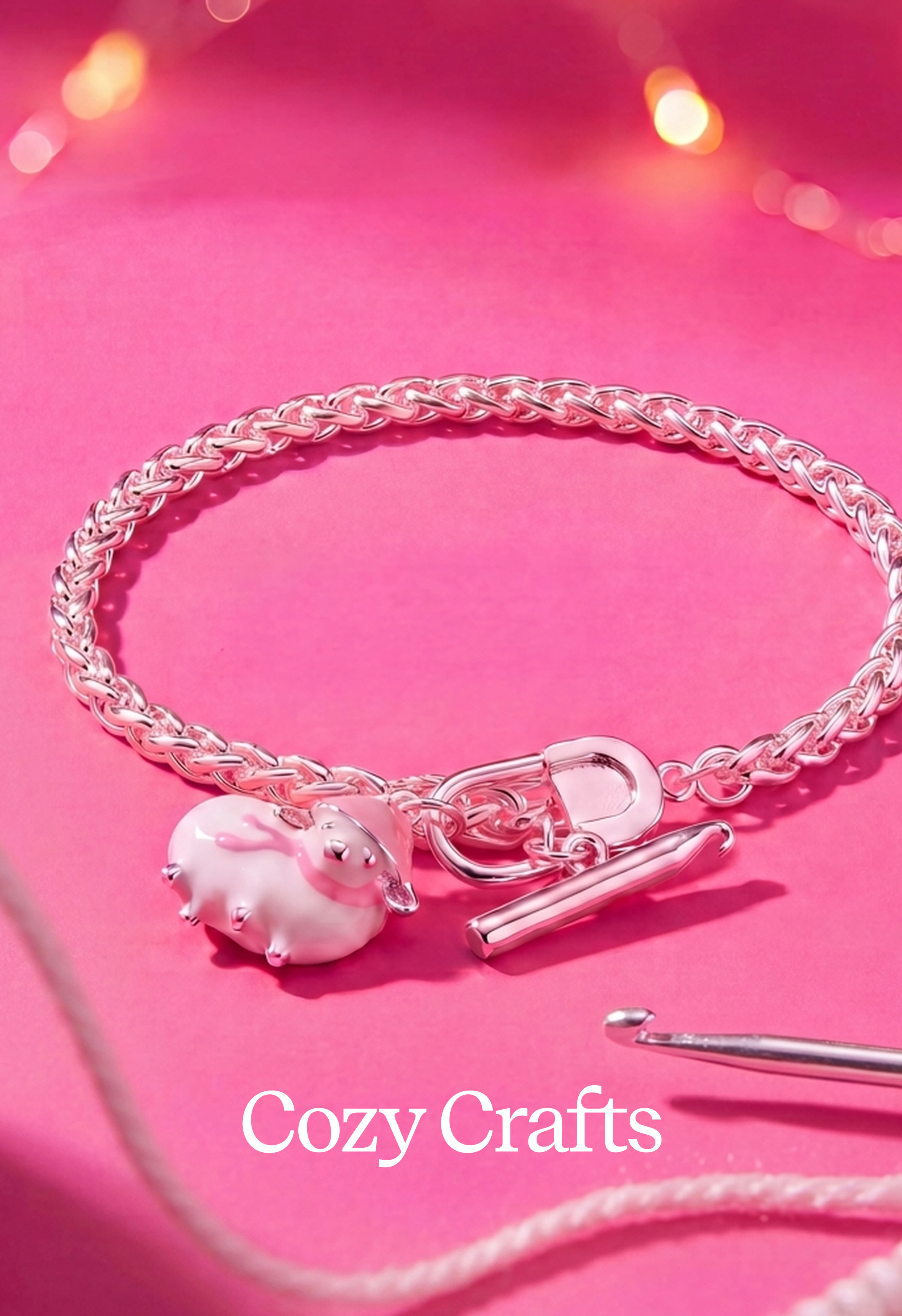 A silver-toned braided chain bracelet with a small pink and white animal charm, shown on a bright pink background with a crochet hook and the text 'Cozy Crafts' visible.