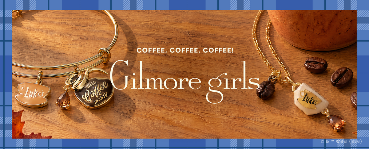 A styled product banner showing two gold charm bracelets on a wooden surface. One bracelet has a bangle-style form with charms including a heart that reads 'Coffee Girl' and a small bag charm reading 'Tule'.