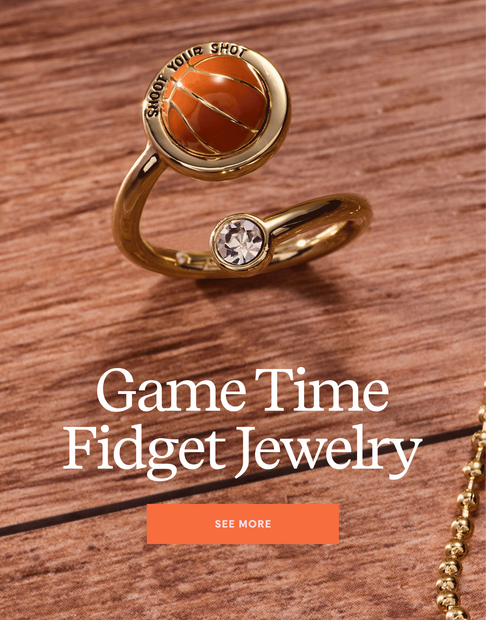 Gold ring with a basketball design on a wooden surface, labeled 'Game Time Fidget Jewelry'.