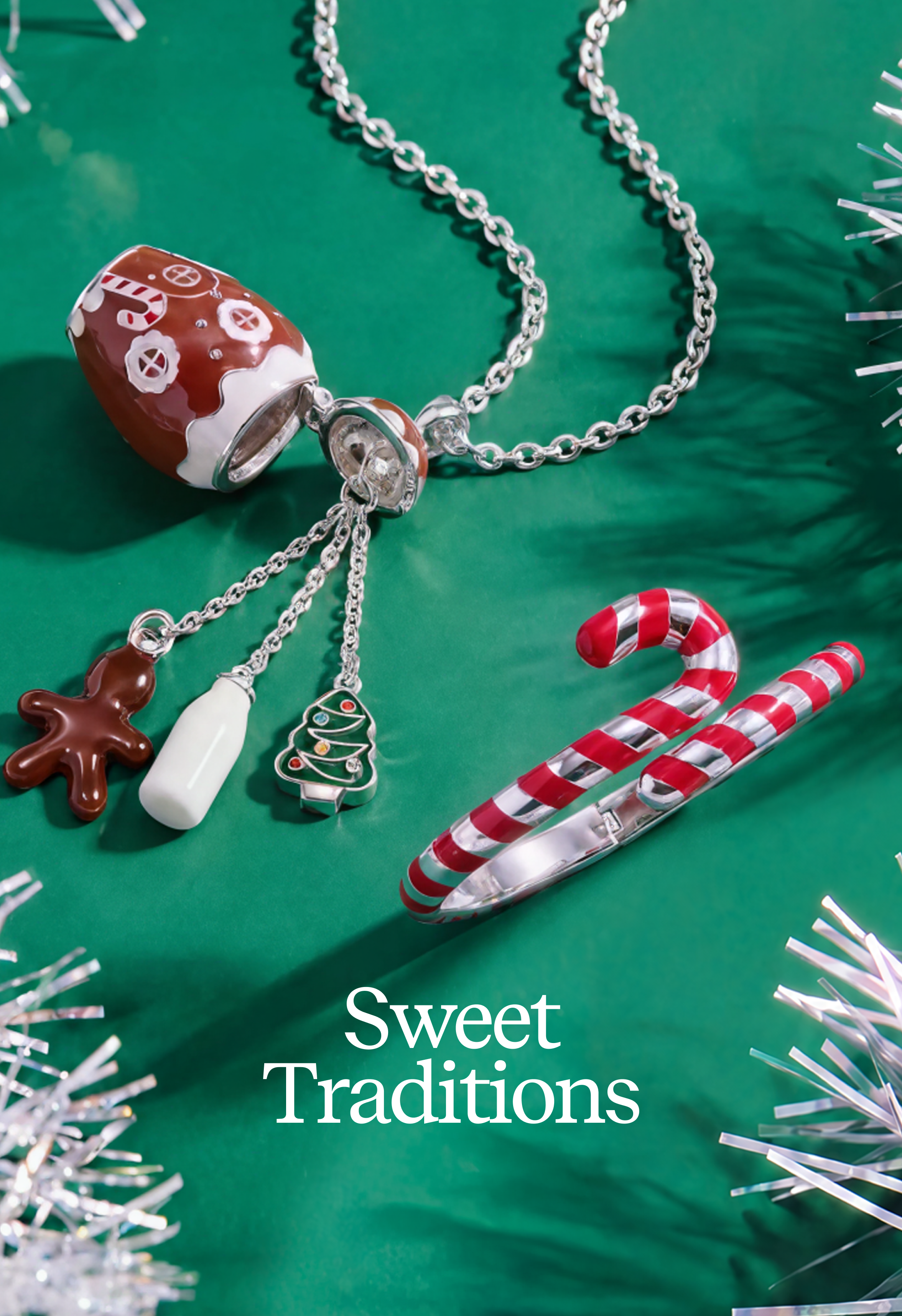 A silver chain necklace with dangling charms, including a gingerbread man, a Christmas tree, a milk bottle, and a brown ornament charm, displayed on a green background with candy canes and tinsel. The text 'Sweet Traditions' is overlaid at the bottom.