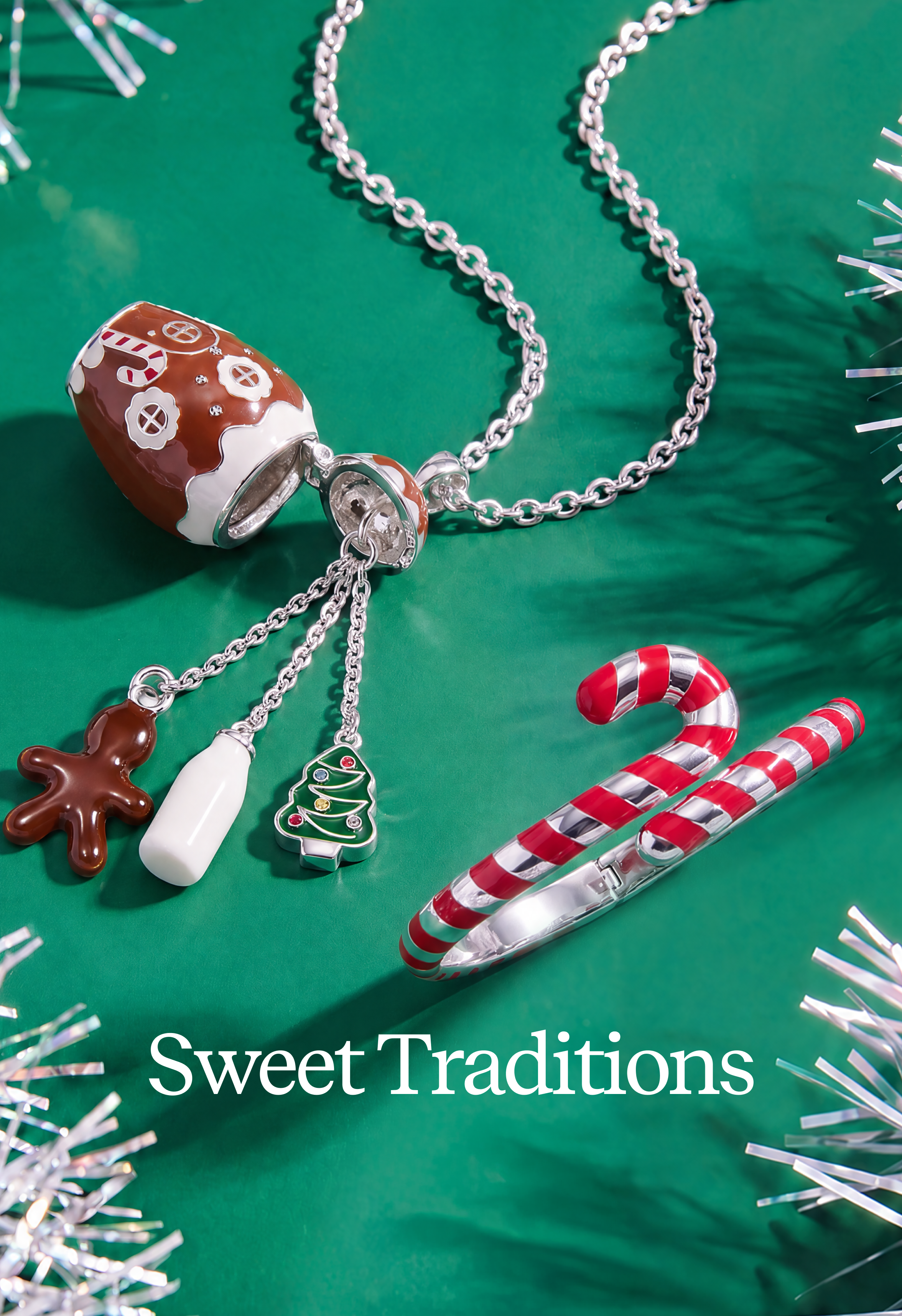 A silver-tone Christmas-themed necklace with dangling charms, including a gingerbread man, a mug, a Christmas tree, and a candy cane, displayed on a green background with tinsel and the text 'Sweet Traditions'.