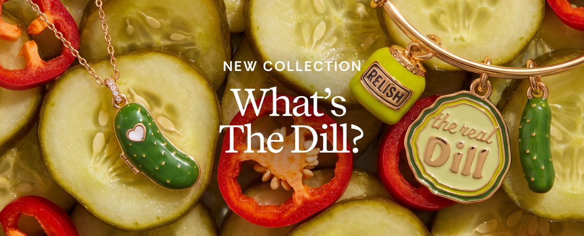 A jewelry collection display featuring enamel charms shaped like pickles and peppers. The collection includes a green pickle pendant on a gold chain with a small heart, a lime green 'RELISH' charm, a round green and yellow 'the real Dill' charm, and a green pickle charm, all styled on sliced cucumbers and red bell peppers with the text 'NEW COLLECTION What's The Dill?' overlaid.