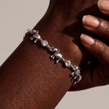 A silver elephant charm bracelet worn on a person's wrist, shown in a close-up shot with warm lighting against a neutral beige background.
