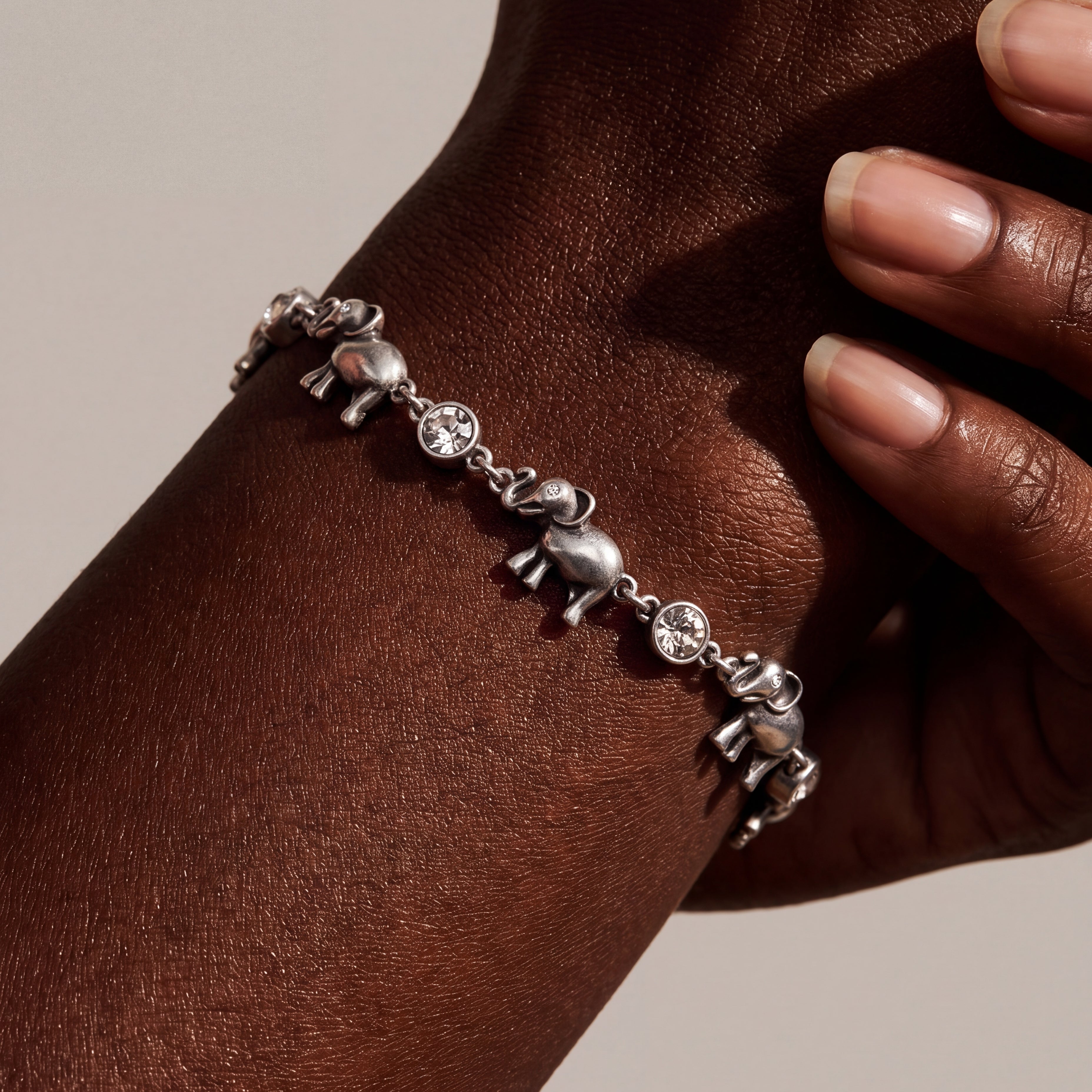 A silver elephant charm bracelet worn on a person's wrist, shown in a close-up shot with warm lighting against a neutral beige background.