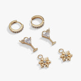 A set of gold-toned jewelry charms and earrings on a light gray background, including two huggie hoop earrings with small clear stones, two martini glass charms with clear stones, and two snowflake charms with clear center stones.