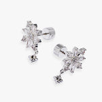A pair of silver snowflake stud earrings with dangling star charms, set with clear crystals on a light gray background.