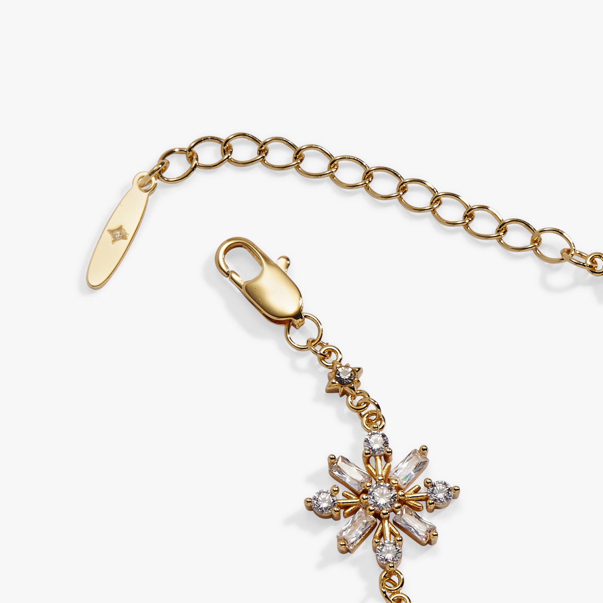 Gold-tone chain extender with lobster clasp and a floral starburst charm set with clear crystals, shown on a light gray background.