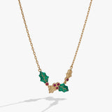 A gold-tone chain necklace featuring a holly pendant with green enamel leaves and small red gemstone accents, shown against a light gray background.