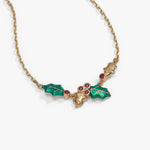A gold-tone chain necklace featuring a holly leaf and berry pendant with green enamel leaves and small red gemstone accents, shown on a light gray background.