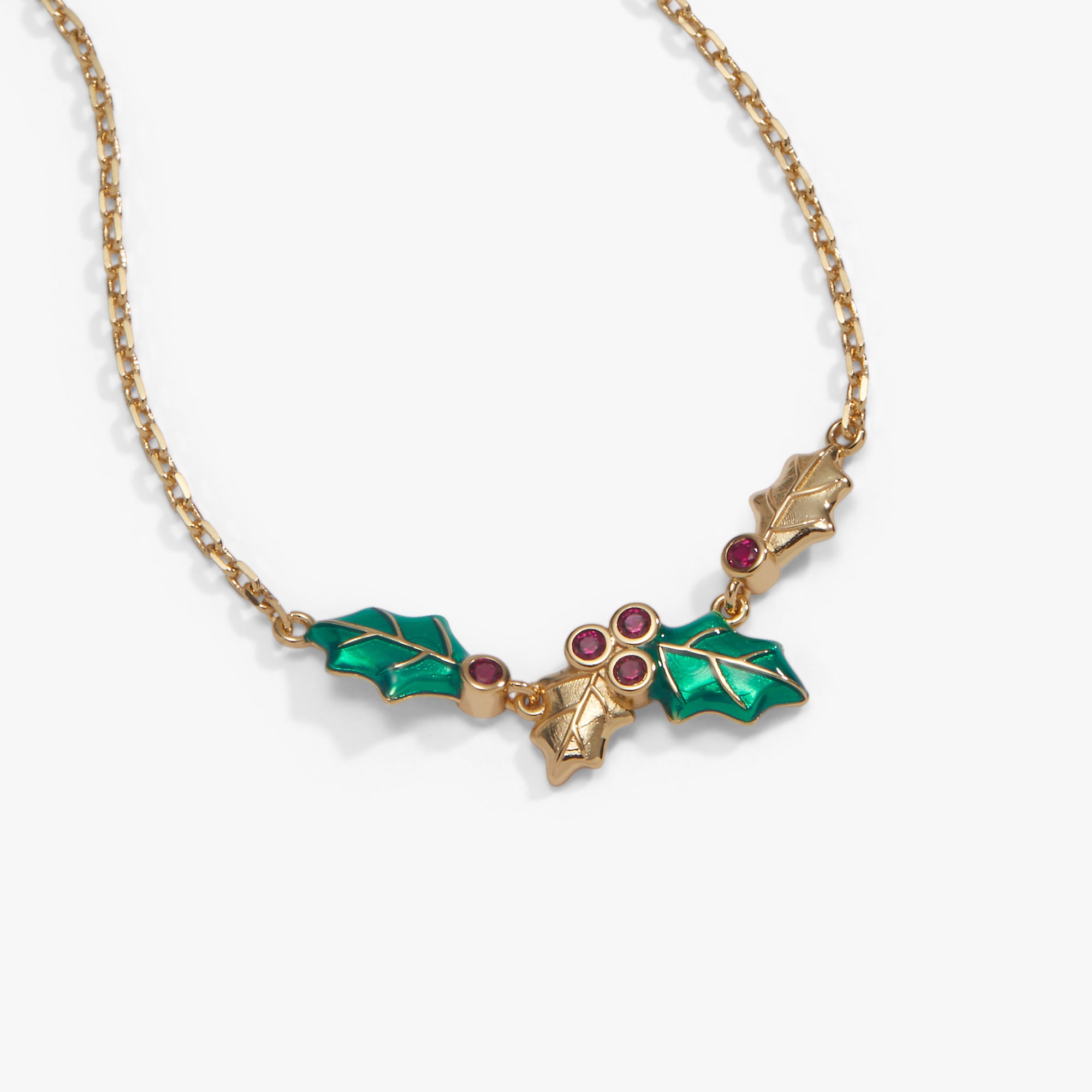 A gold-tone chain necklace featuring a holly leaf and berry pendant with green enamel leaves and small red gemstone accents, shown on a light gray background.