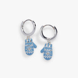 A pair of silver huggie hoop earrings with dangling light blue mitten charms decorated with white snowflake patterns, shown on a light gray background.